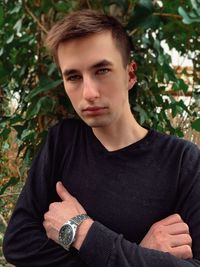 Portrait of young man standing by tree outdoors