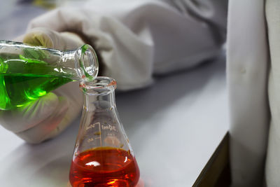 Cropped hand of person pouring chemical in beaker on table