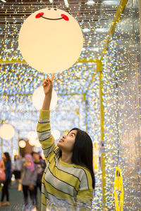 Young woman touching balloon while standing in illuminated corridor