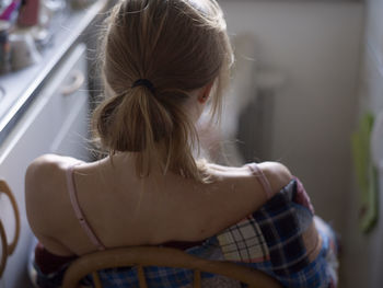 Young woman sitting in kitchen, rear view