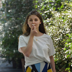 Portrait of beautiful young woman standing against trees