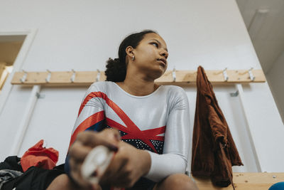 Contemplative teenage girl wearing sports clothing sitting in locker room