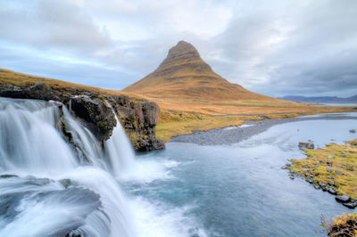 River flowing through rocks against cloudy sky