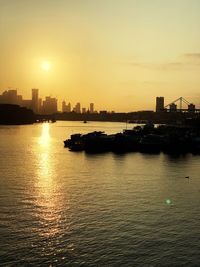 Silhouette buildings by sea against sky during sunset