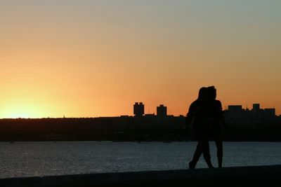 Silhouette man standing by cityscape against sky during sunset
