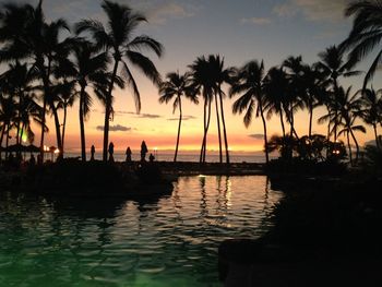 Silhouette palm trees by swimming pool against sky during sunset