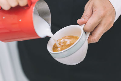 Midsection of man pouring milk in coffee