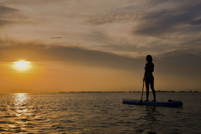 Silhouette woman paddle boarding on sea against sky during sunset