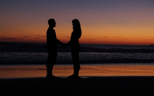 Silhouette couple standing at beach during sunset