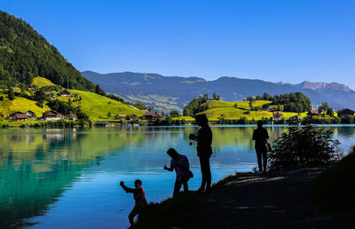 Silhouette people by lake against mountains and clear sky