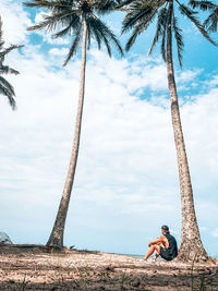 Low section of man on palm tree against sky