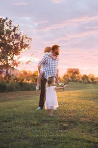 Father and daughters on grass against sky during sunset