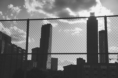 Low angle view of silhouette fence by buildings against sky