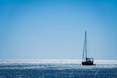 Sailboat sailing in sea against clear blue sky