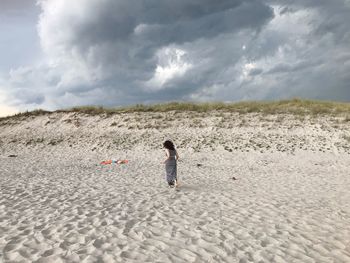 Rear view of woman running on sand at beach against cloudy sky