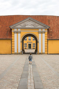 Rear view of boy walking on building against sky