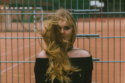 Portrait of young woman with tousled hair against fence