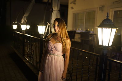 Woman standing by railing in illuminated room