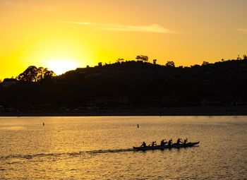 Silhouette people sailing on river against sky during sunset