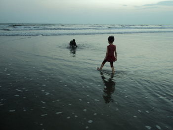 Rear view of boys at beach against sky