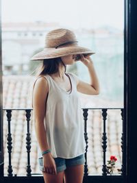 Young woman on the balcony wearing summer clothes and a hat