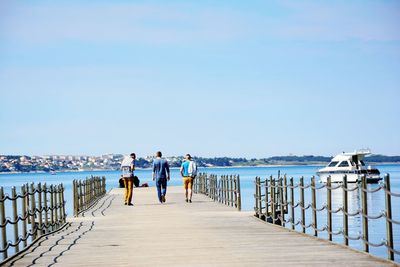 Rear view of friends walking on pier against sky