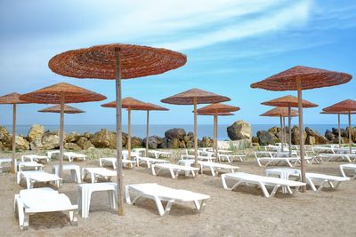 Lounge chairs and tables on beach against sky