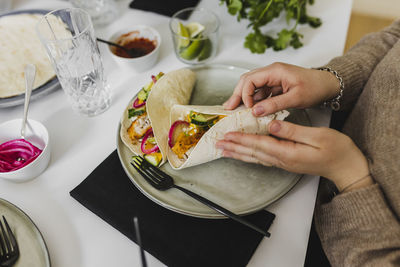 Person wrapping mexican tortilla with various toppings