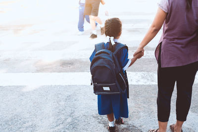 Rear view of mother holding daughter hand while walking on street