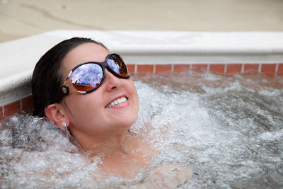 Young adult woman brunette lounging in hot tub with sunglasses smiling with bubbles