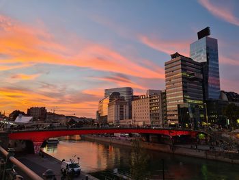 Bridge over river by buildings against sky during sunset