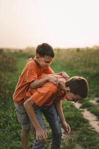 Funny boys brothers in a orange t-shirt playing outdoors on the field at sunset