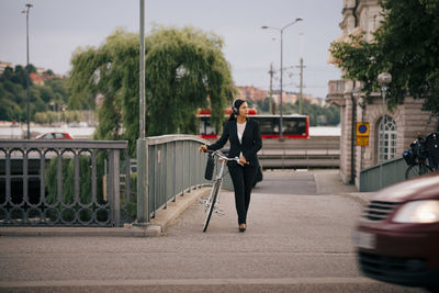 Businesswoman looking away while walking with bicycle on bridge in city