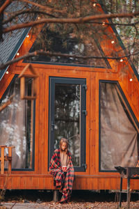 Full length of girl sitting against wooden house