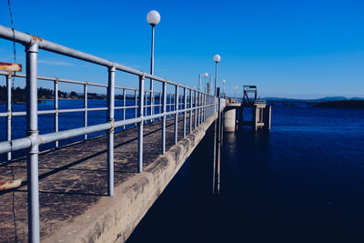 Pier on sea against clear blue sky