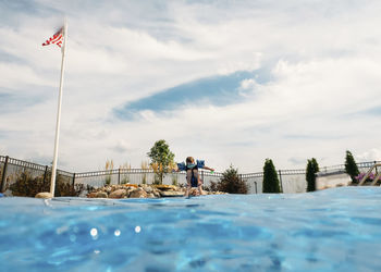 Surface level of father lifting boy in swimming pool against sky