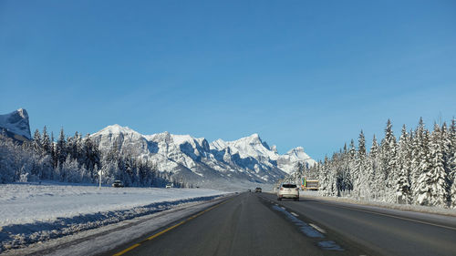 Road amidst snowcapped mountains against clear blue sky