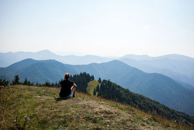 Rear view of man sitting on mountain against sky