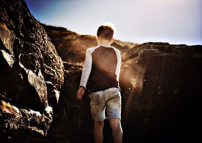 Rear view of man standing on rock against sky