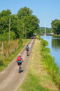 People riding bicycle on road by canal