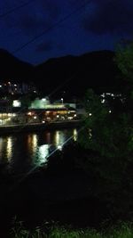 Illuminated buildings by river against sky at night