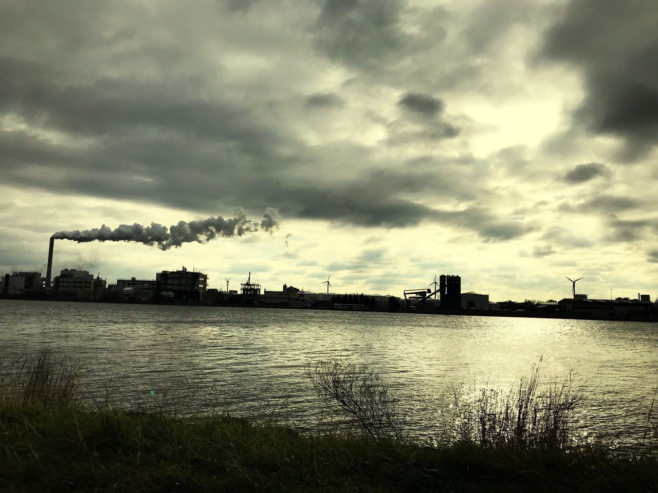 RIVER BY FACTORY AGAINST CLOUDY SKY