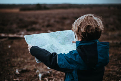 Rear view of boy holding map while standing on field