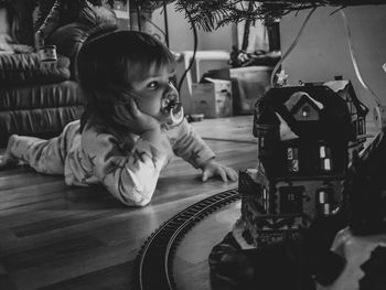 Cute girl sucking pacifier while looking at toy in home