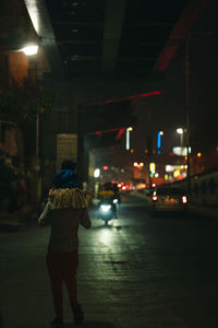 Rear view of man walking on illuminated street at night