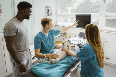 Male doctor showing ultrasound of dog on computer screen to owner in medical clinic