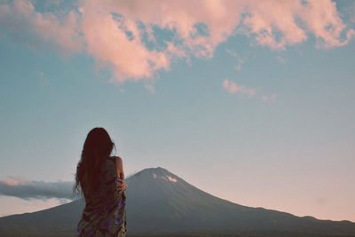 Rear view of woman standing against mountain during sunset