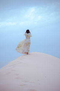 Rear view of woman standing on beach against sky