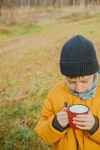 Boy drink hot chocolate from cups in the forest. boy in a yellow jacket are holding hot cocoa.