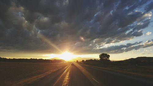 Road passing through field against cloudy sky